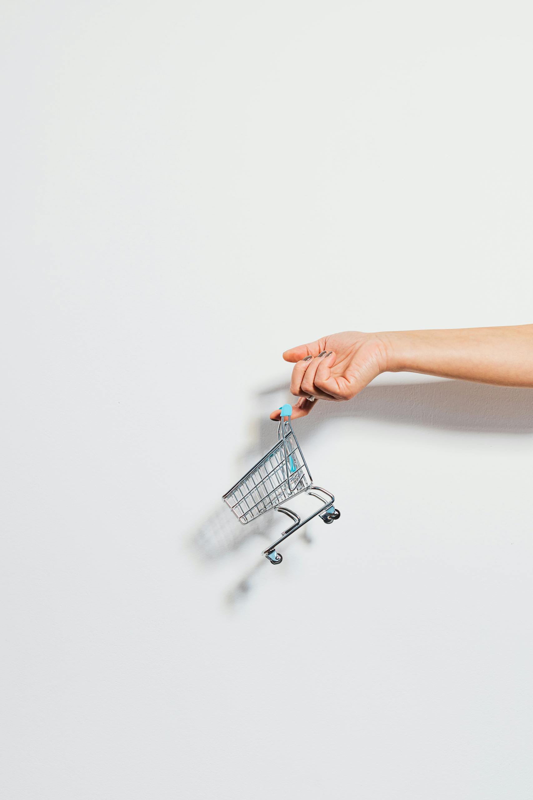 A hand holding a miniature shopping cart against a clean white background, emphasizing simplicity.