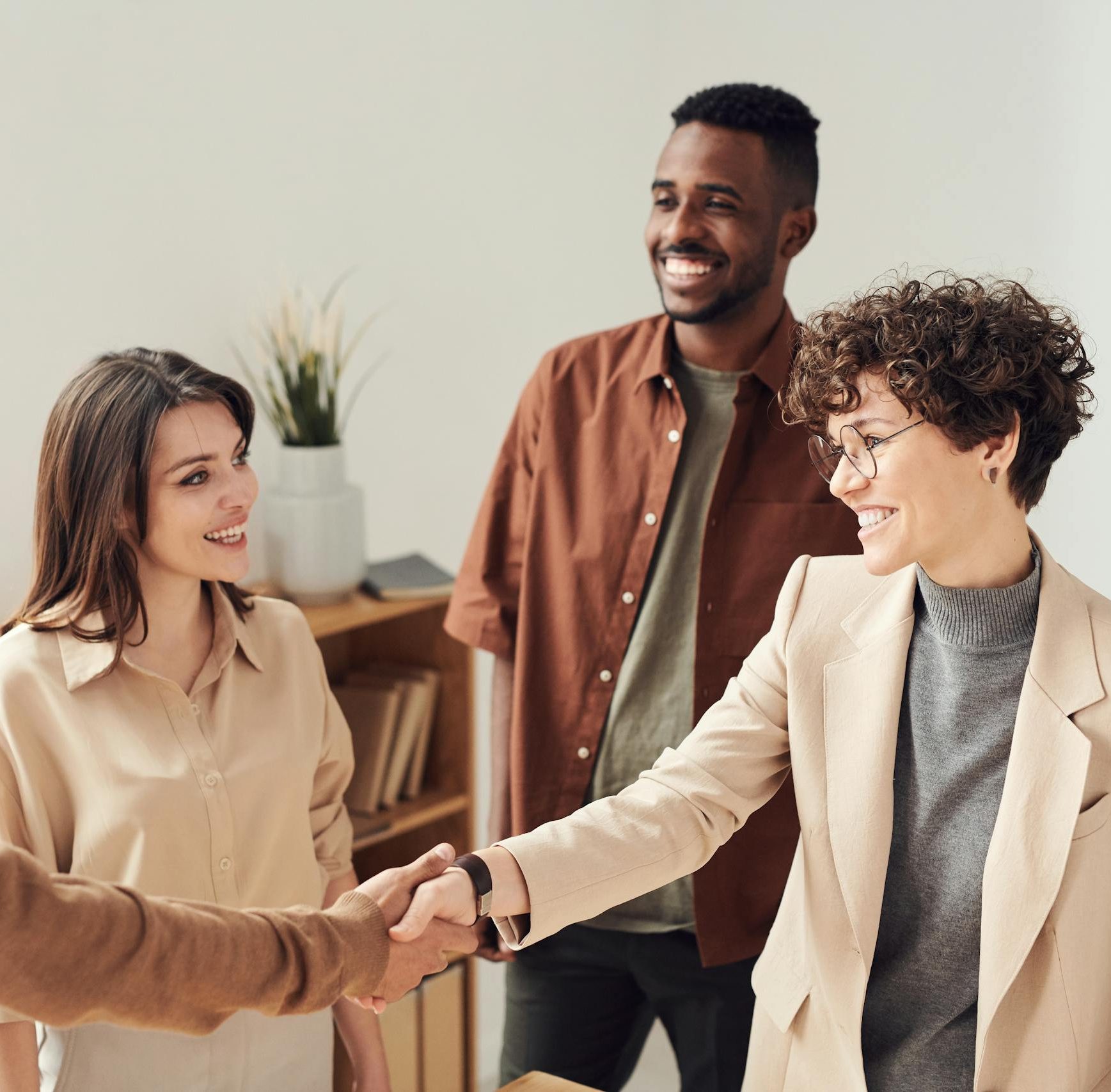 Four colleagues smiling and shaking hands in a bright office setting.