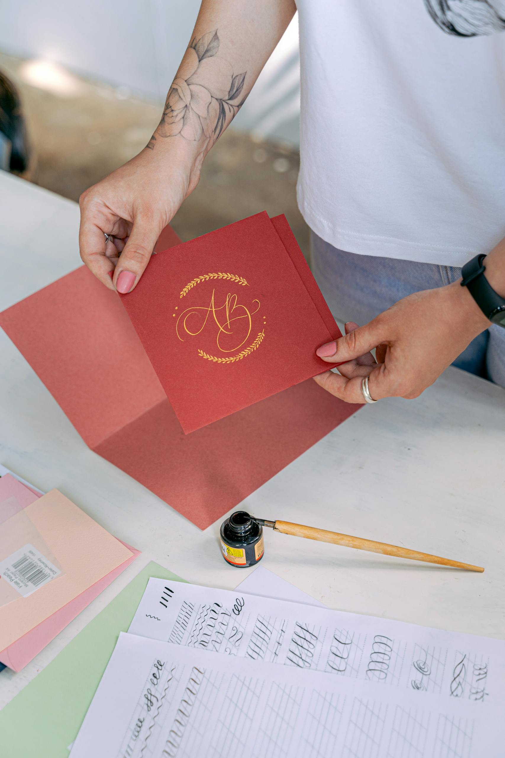 Person crafting a handmade invitation with calligraphy details, featuring a red card and ink.