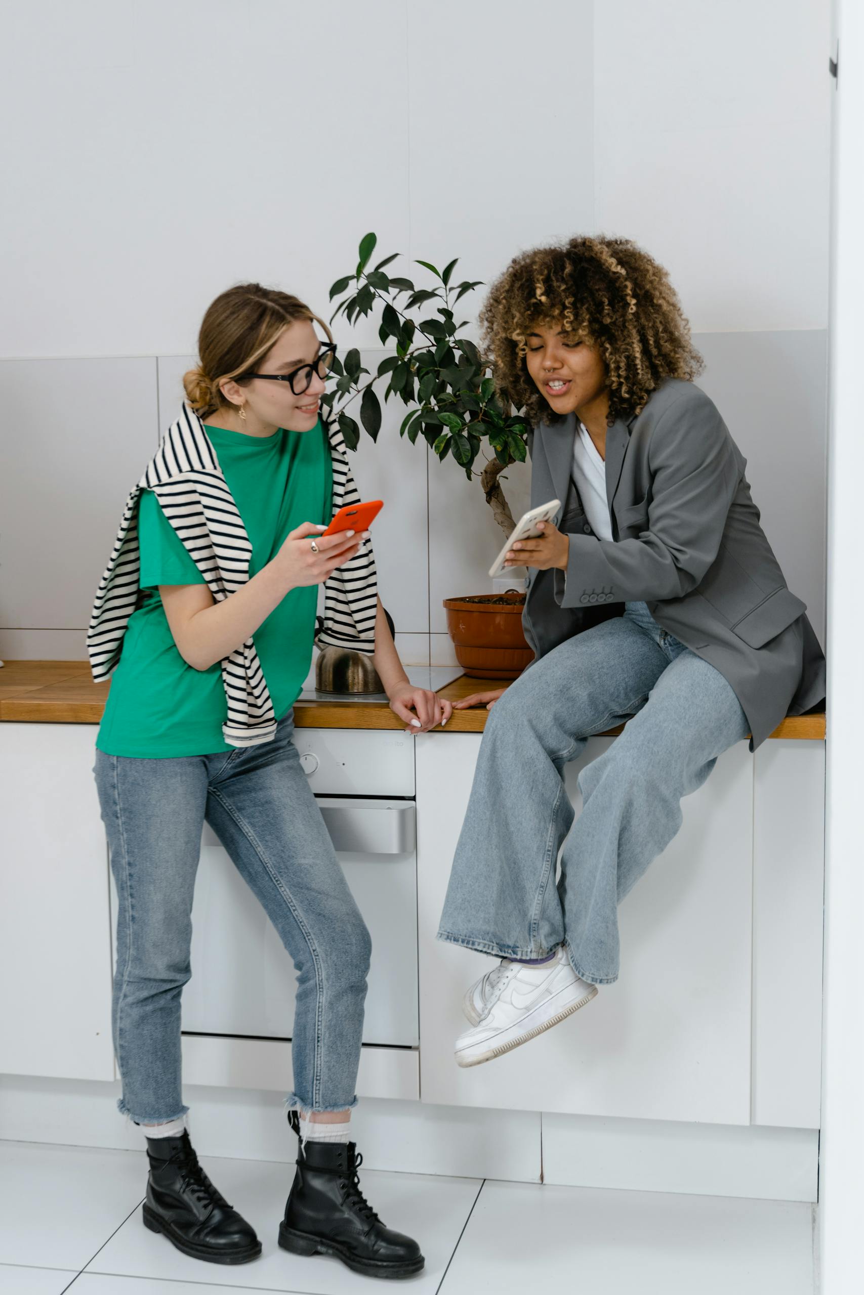 Two women in casual attire discussing ideas with smartphones in a modern office.